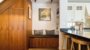 A kitchen with wooden cabinets, a bench with patterned cushions, and a bar stool. - Welcome to your stylish retreat in the heart of Primrose Hill (London)