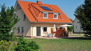 Una casa de dos pisos con techo inclinado, un pequeño balcón y un patio con mobiliario exterior.