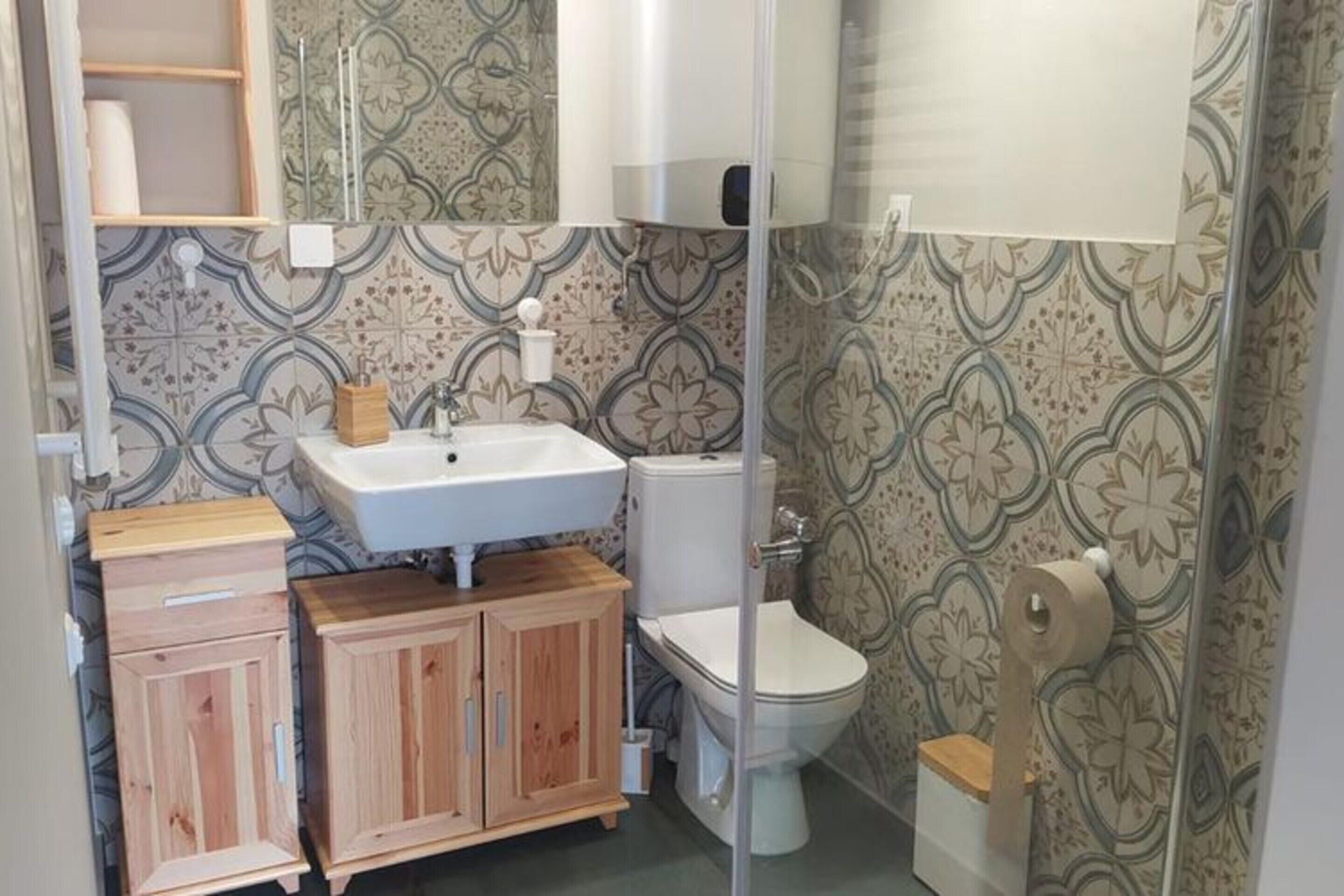 A compact bathroom with a wooden vanity, a white sink, a toilet, and a shower area.