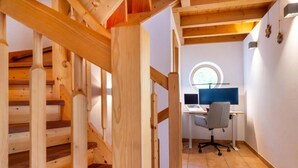 Un escalier en bois mène à une pièce où se trouvent un bureau, une chaise et une fenêtre ronde.