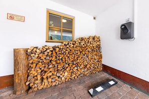 Une pile de bois de chauffage est appuyée contre un mur, juste en dessous d’une fenêtre.