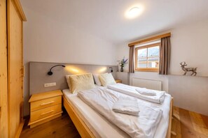 Ein Schlafzimmer mit einem Bett, Nachttischen, einer Wandlampe, einem Fenster mit Vorhängen und einer kleinen Dekoration mit einem Reh.