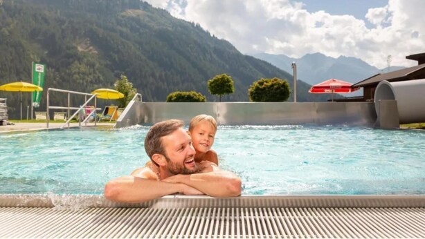 Une piscine avec une chaîne de montagnes en arrière-plan, un poste de surveillance pour les sauveteurs et des parasols.