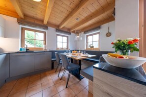 A modern kitchen with a dining area, wooden ceiling beams, and large windows. - Stylish Ten-person Alpine Chalet (Wald im Pinzgau)