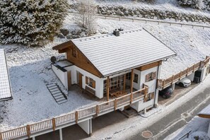 Un chalet à deux étages doté d’un balcon, d’une véranda et d’une voiture garée dans l’allée.