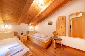 A room with wooden floors, a bed, a chair, a nightstand, and a wall-mounted mirror. - Stylish Ten-person Alpine Chalet (Wald im Pinzgau)