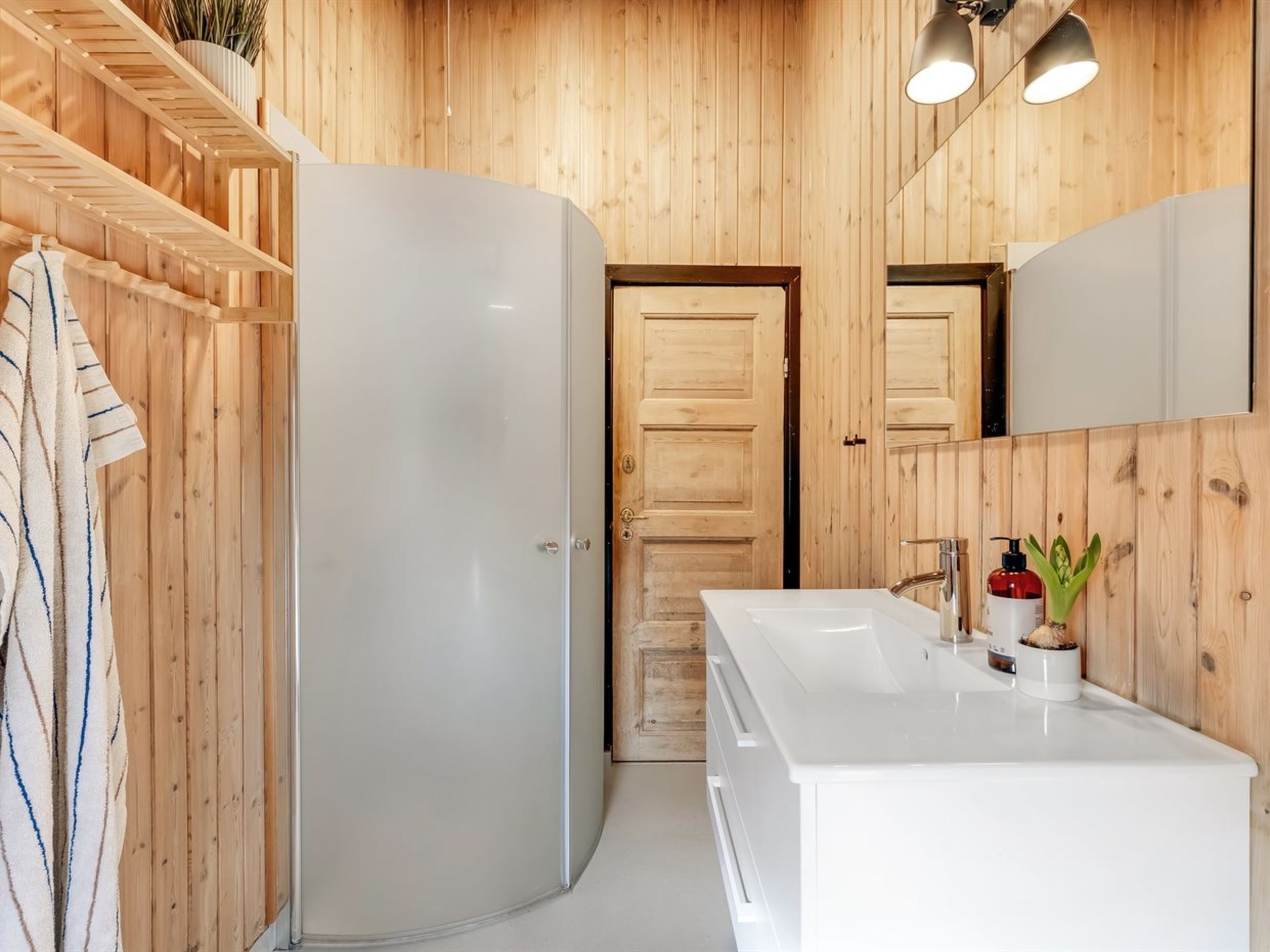 A bathroom with wooden paneling, a white sink, a mirror, and a towel rack.