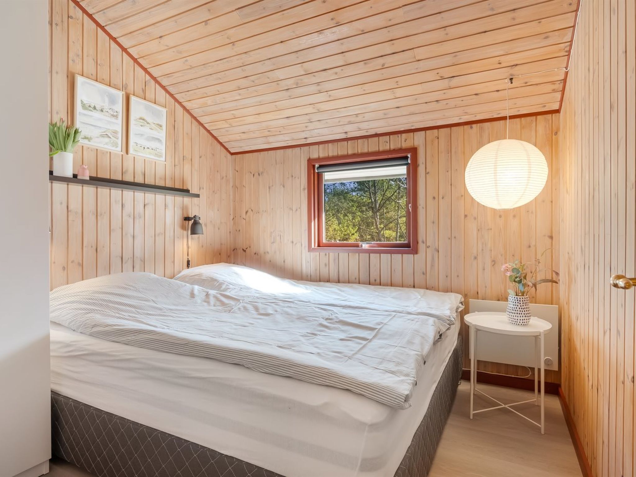 Une chambre à coucher avec un lit, une fenêtre, une table de chevet et un luminaire suspendu.
