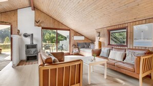Ein gemütliches Blockhaus mit Schlafzimmer im Obergeschoss, einem Wohnbereich inklusive Sofa und Couchtisch sowie einem Holzofen.