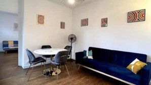 A modern living room with a blue sofa, a dining table with chairs, and a ceiling fan. - Apartment Saphir (5) 2/6 pers (Sedan)