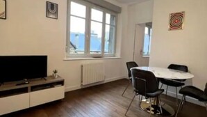 A modern living room with a flat-screen TV, wooden flooring, a dining table with chairs, a large window with a view, and a ceiling light fixture. - Apartment Saphir (5) 2/6 pers (Sedan)