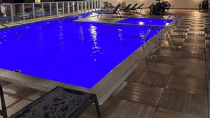 A swimming pool with a blue tint, surrounded by lounge chairs and umbrellas, and a wooden deck area. - Complete apartment with pool in Itajaí (Dom Bosco Itajaí)