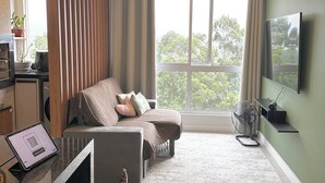 A modern living room with a sofa, a dining area with a tablet, a TV, and a large window with a view of trees. - Complete apartment with pool in Itajaí (Dom Bosco Itajaí)