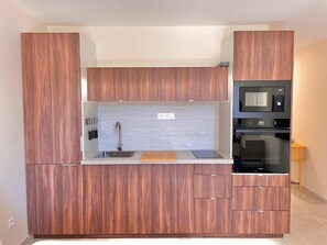 A modern kitchen with wooden cabinetry, a built-in microwave, and a double oven. - Le Travolta avec merveilleuse terrasse (Cannes)