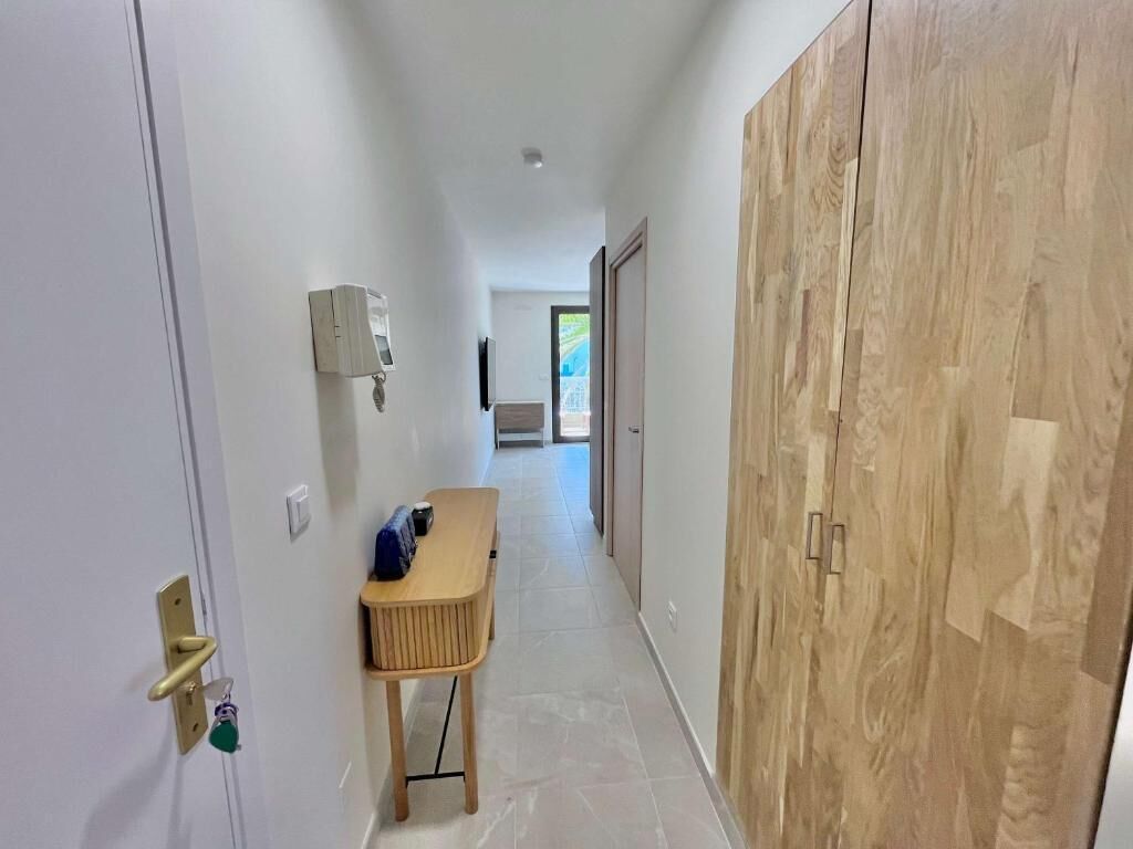 Un couloir avec une armoire en bois, une petite table avec des chaises et un luminaire fixé au mur.