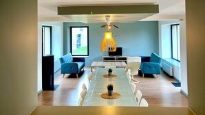 A modern dining area with a long table, blue sofas, and a unique hanging light fixture. - Maison des H, by the lake (CANISY)
