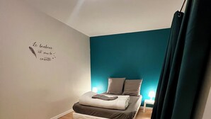 A modern bedroom with two beds, wooden flooring, teal accent walls, and a wall-mounted light fixture. - Maison des H, by the lake (CANISY)