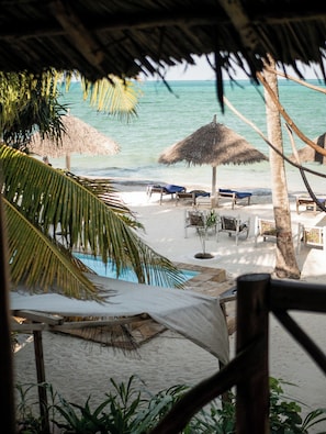 A beach with thatched umbrellas, lounge chairs, and a pool area. - Villa Bahati Zanzibar (Jambiani)