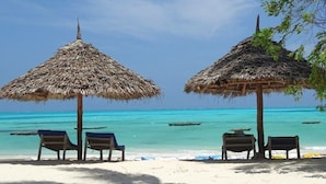 A beach with two thatched umbrellas and lounge chairs. - Villa Bahati Zanzibar (Jambiani)