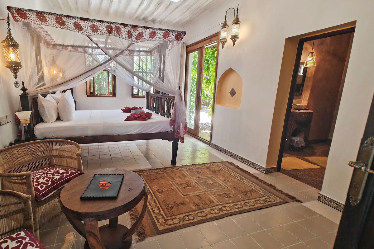 A bedroom with a bed, a chair, a small table, and a door leading outside.
