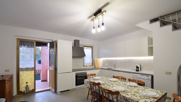 Una cocina moderna con armarios blancos, una mesa de comedor para cuatro personas y un amplio ventanal con vistas a un balcón.