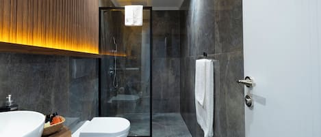 A modern bathroom with a glass shower enclosure, a white toilet, and a vanity with a large sink and a basket of toiletries.