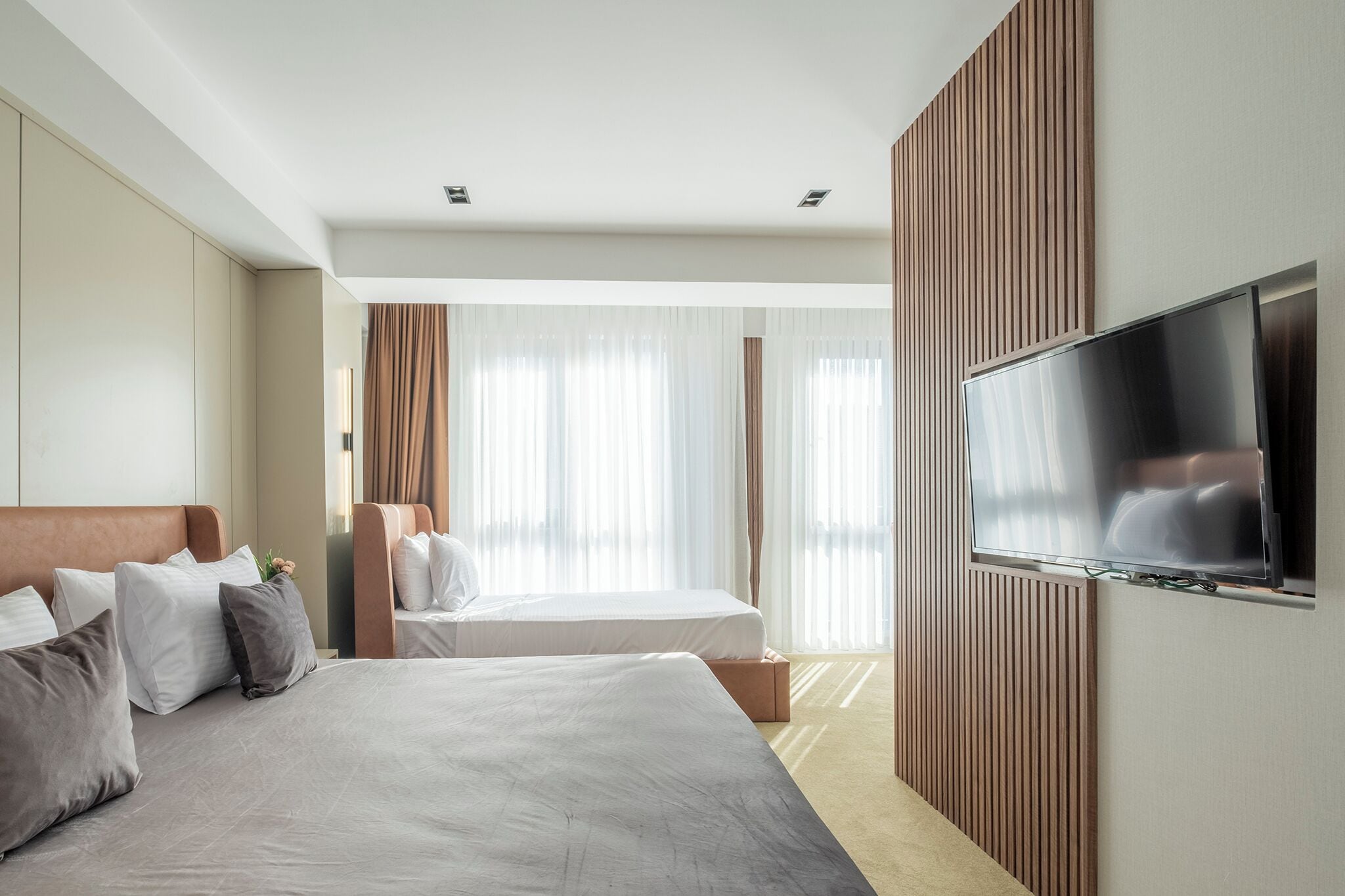 A modern hotel room with a large bed, a TV mounted on the wall, and a large window with curtains.