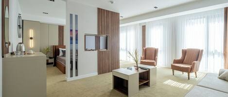 Habitación de hotel moderna con sofá, sillones, una mesa de centro, televisor y escritorio con lámpara.