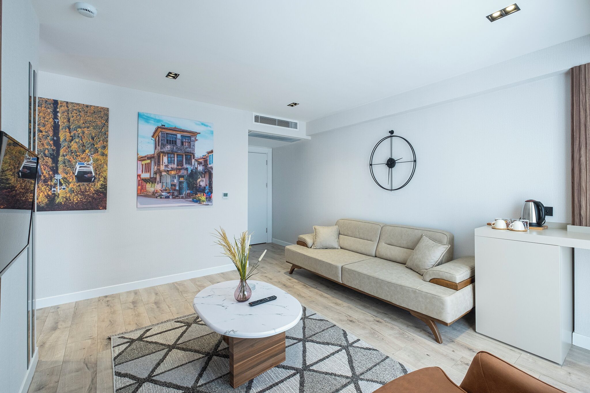 A modern living room with a sofa, a coffee table, and a TV. There are two paintings on the wall and a clock.