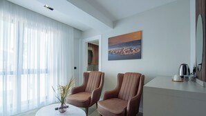 A modern hotel room with two leather armchairs, a round marble table, a painting of a coastal city, and a large window with sheer curtains. - EUPHRATES HOTEL (Bursa)