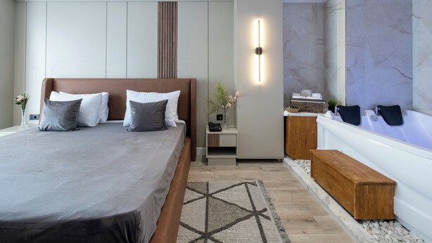 A modern bedroom with a large bed, a bedside table with a lamp, a small seating area, and a wall-mounted light fixture. - EUPHRATES HOTEL (Bursa)