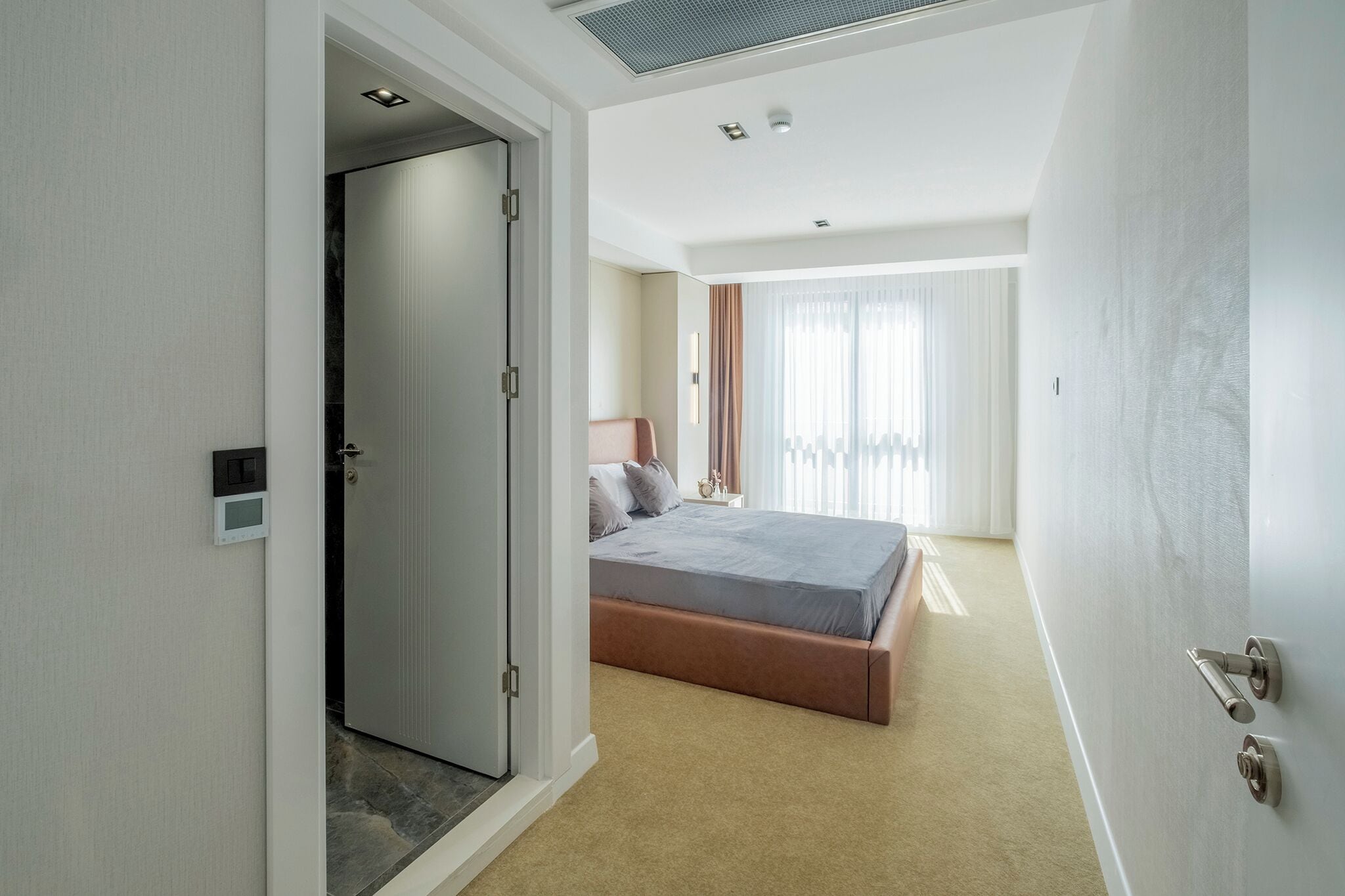 A hotel room with a bed, a door, and a window.