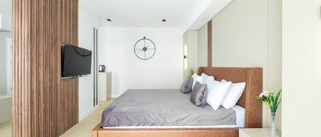 A modern bedroom with a wooden accent wall, a large bed with grey bedding, a wall-mounted TV, and a minimalist design.