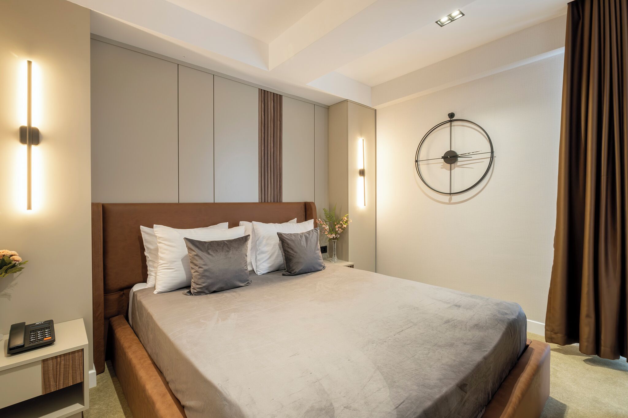 A modern bedroom with a large bed, bedside tables, wall-mounted lights, and a clock.