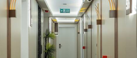 A hotel hallway with a ceiling exit sign, a door labeled "503", and a potted plant.