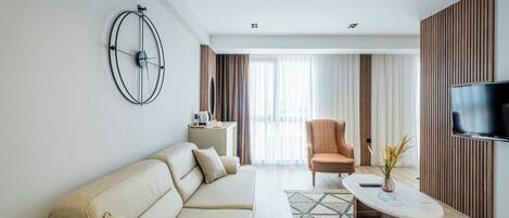 Una sala de estar moderna con un sofá color beige, una mesa de centro, un televisor montado en la pared y un ventanal con cortinas.