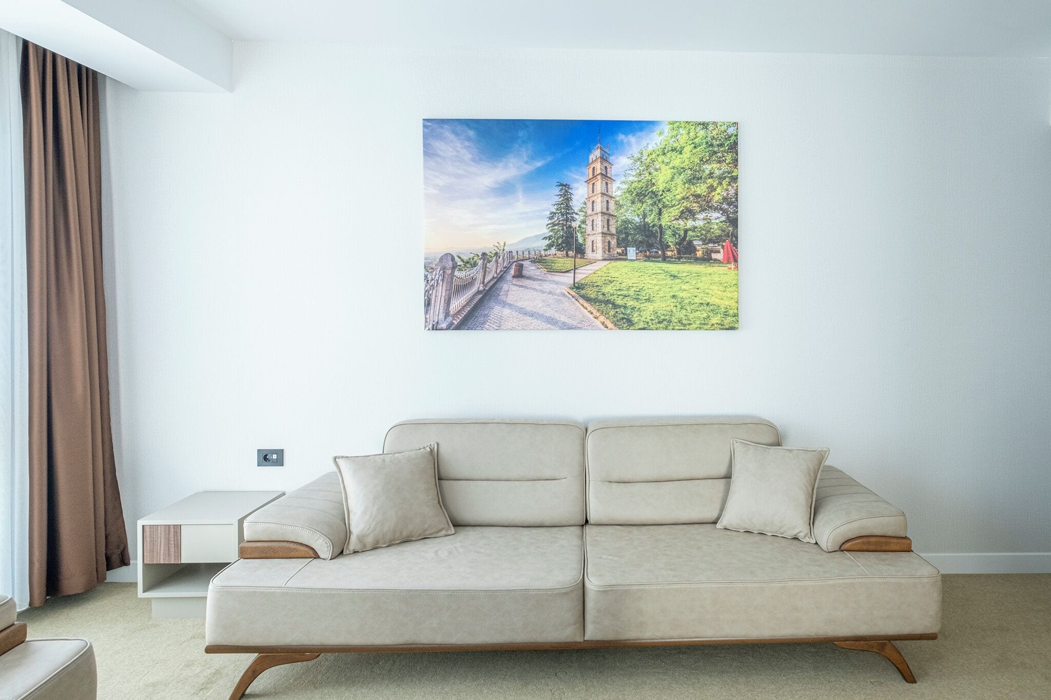 Ein modernes Wohnzimmer mit einem beigen Sofa, einem kleinen Beistelltisch und einem großen Landschaftsbild an der Wand.