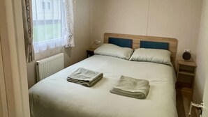 Ett sovrum med en säng, två kuddar, ett nattduksbord, en lampa och ett fönster med gardiner.