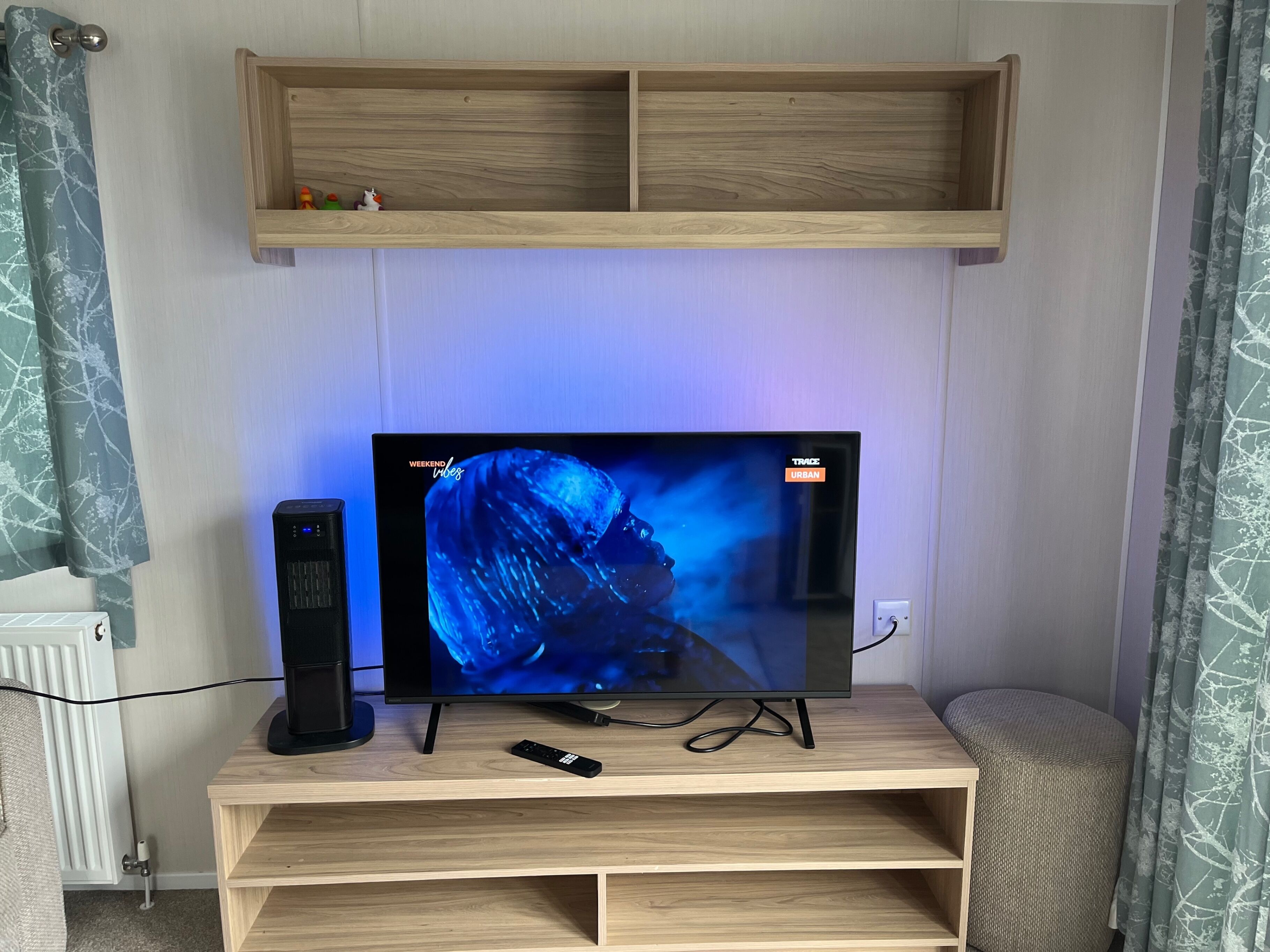 Un téléviseur posé sur un meuble en bois, avec une étagère au-dessus.