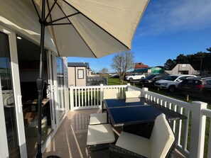 A balcony with a table and chairs, a white fence, and a view of parked cars and buildings. - Surfside Bliss - Cayton Bay Park Caravan (Scarborough)
