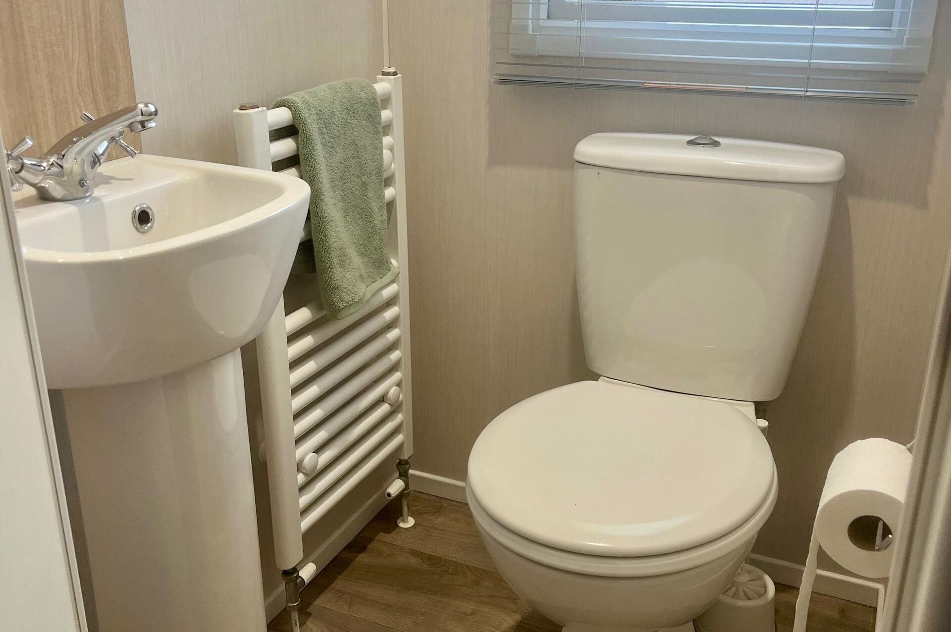 Ein kleines Badezimmer mit Waschbecken, Toilette und Heizkörper, alles in Weiß.