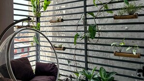 Ein modernes Interieur mit einem Hängekorbstuhl, einer Betonwand mit Pflanzen und Blick durch ein Fenster.