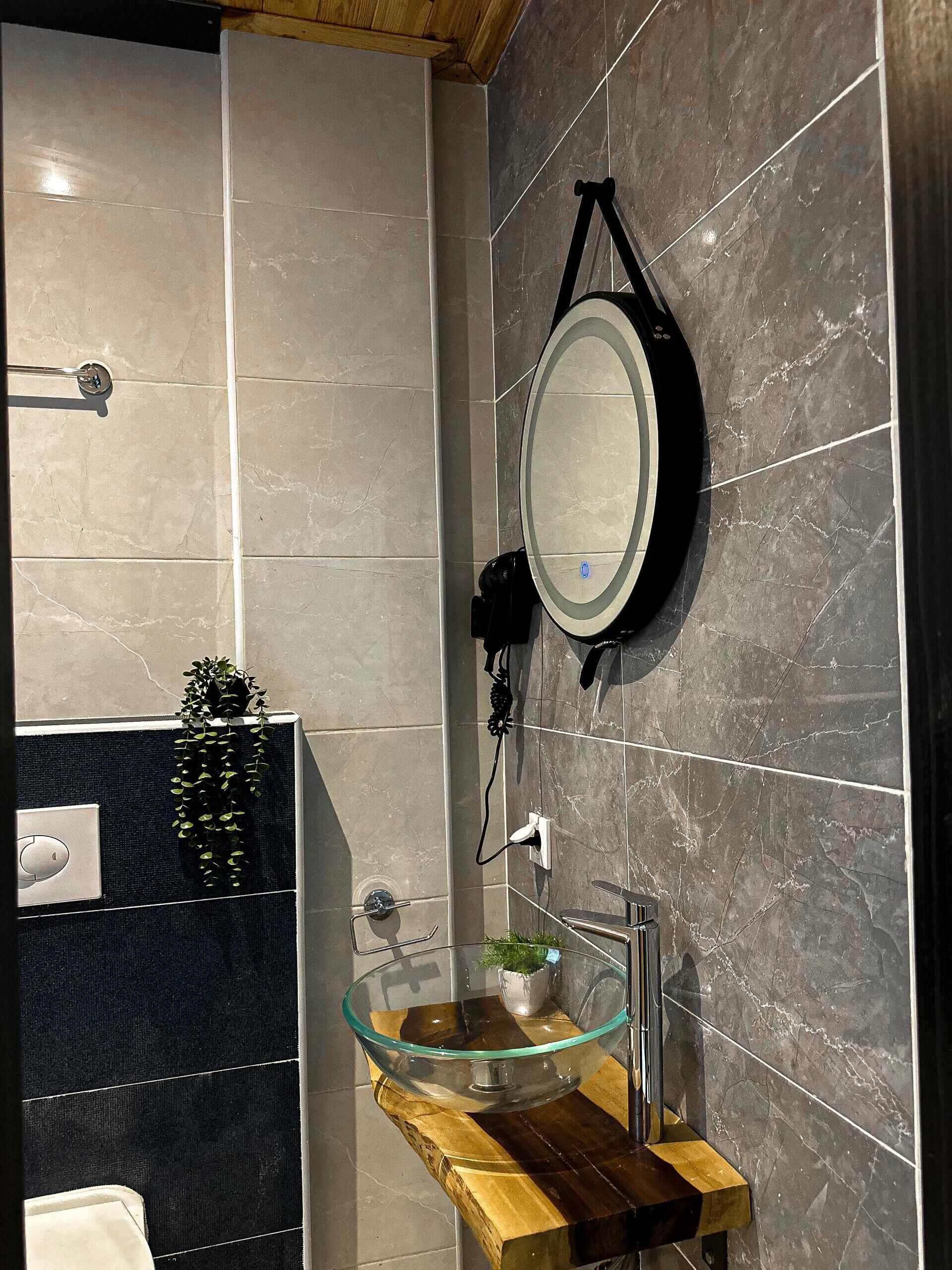 A modern bathroom with a glass bowl sink, a black wall-mounted mirror, and a wooden vanity.