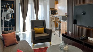 Ein modernes Wohnzimmer mit Sofa, Sessel und Couchtisch, ein Essbereich mit Stühlen und eine Küche im Hintergrund.