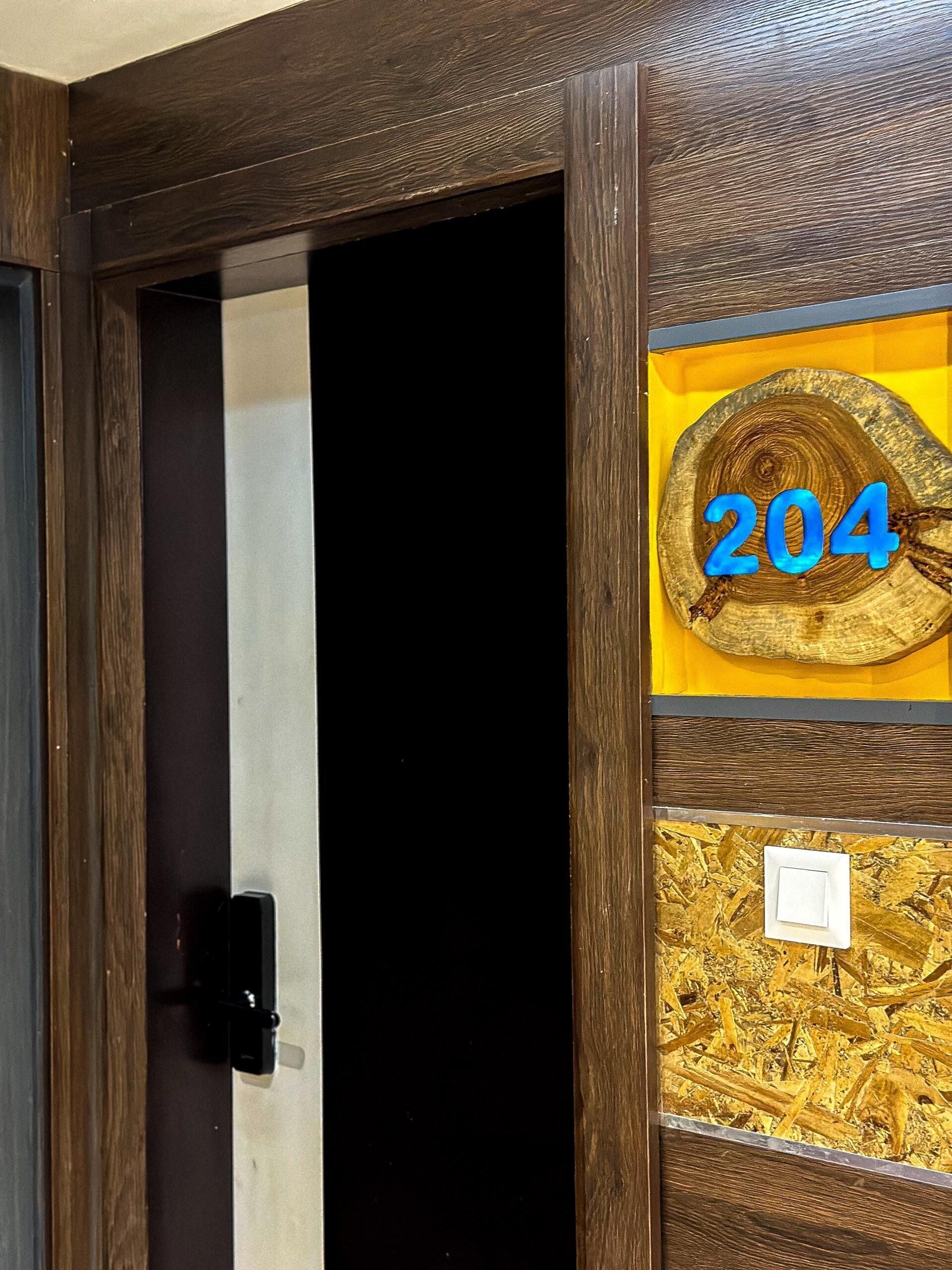 A wooden door with a black handle, a number '204' on a yellow background, and a small white switch on the door frame.