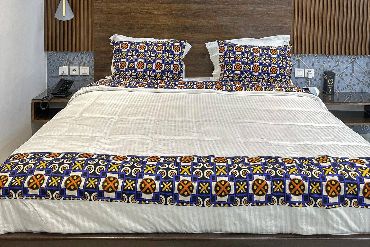 A modern bedroom with a large bed, patterned bedding, a wooden headboard, and a bedside table with a phone.