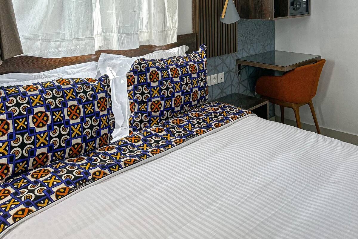 A modern hotel room with a large bed, a desk, and a mirror.