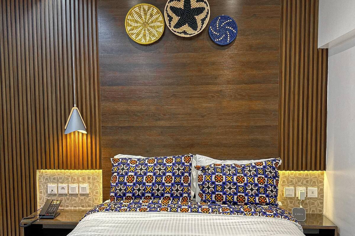 A modern bedroom with a large bed, patterned pillows, a bedside table with a lamp, and a wall with three decorative plates.