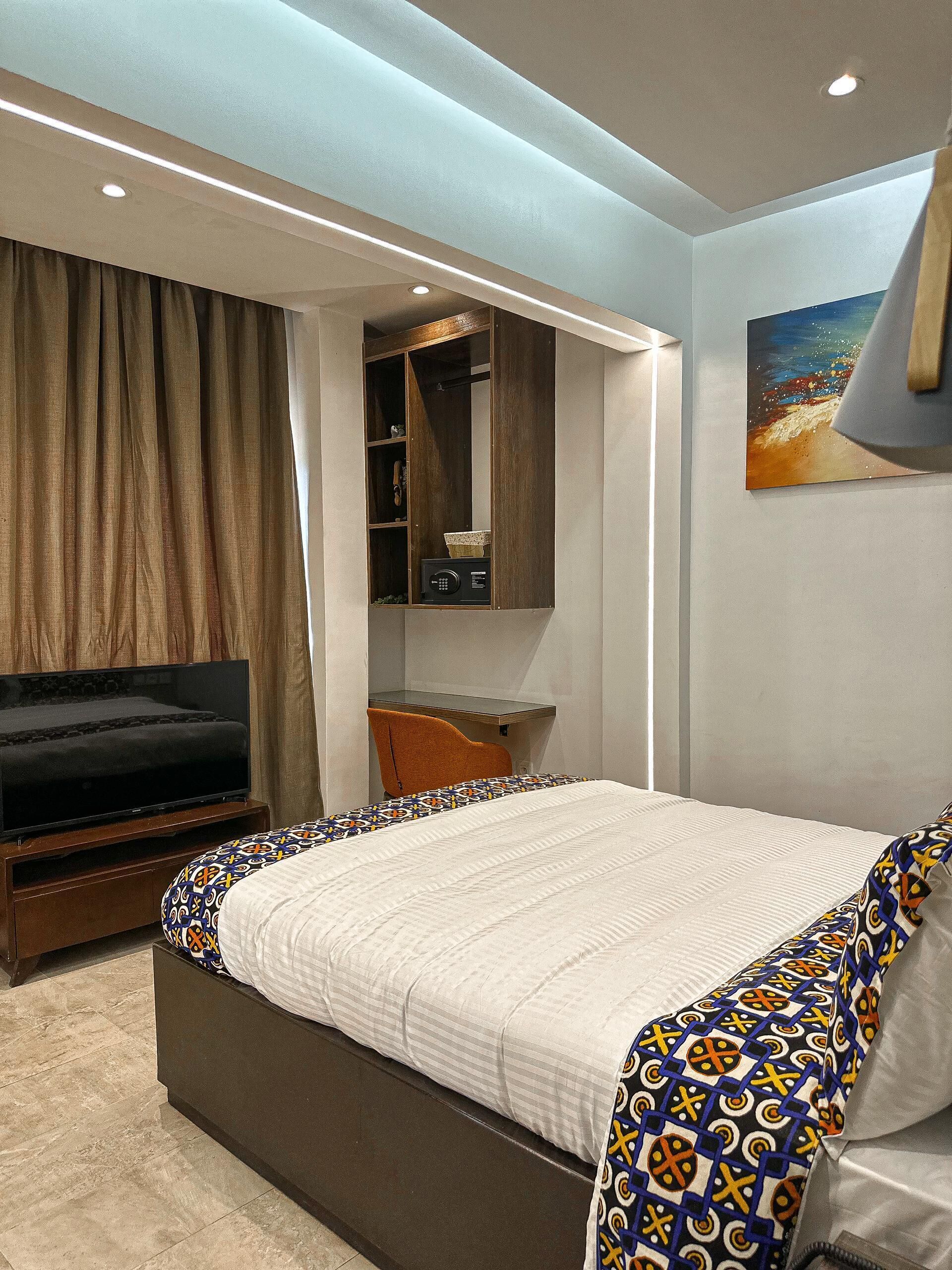 A modern bedroom with a bed, a TV, a desk, and a wardrobe.