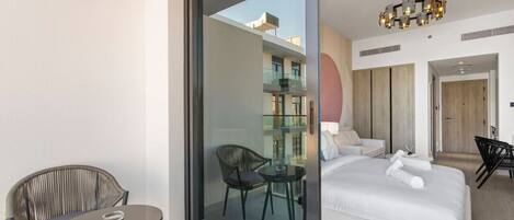 A modern hotel room with a balcony, a bed with white linens, a glass door leading to a balcony, and a contemporary chandelier.